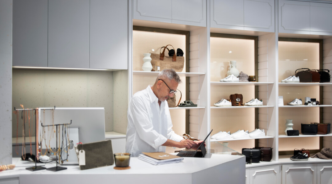 Un homme en chemise blanche travaille sur un ordinateur portable, entouré d'étagères, concentré sur la conception d'une rénovation de cuisine haut de gamme.