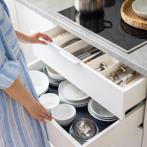 A woman organizes plates and cutlery in a drawer, highlighting the importance of storage furniture.